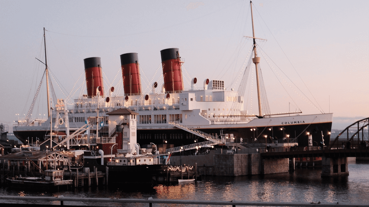 Large ship "Columbia" with red funnels, docked at sunset, adorned with string lights.