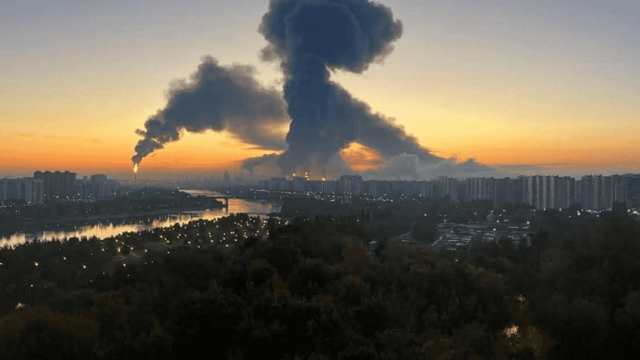 Large smoke plume over cityscape at sunrise with river and buildings.