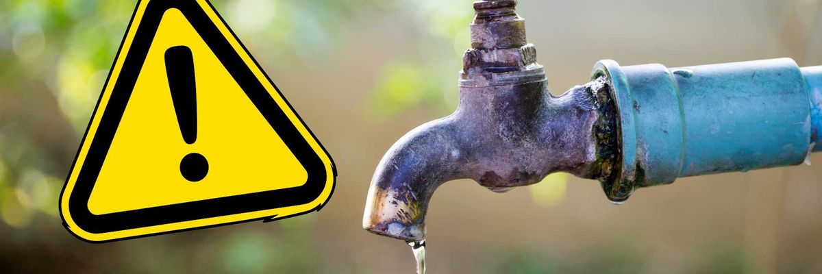 Leaking faucet with a warning sign, outdoor blurred background.