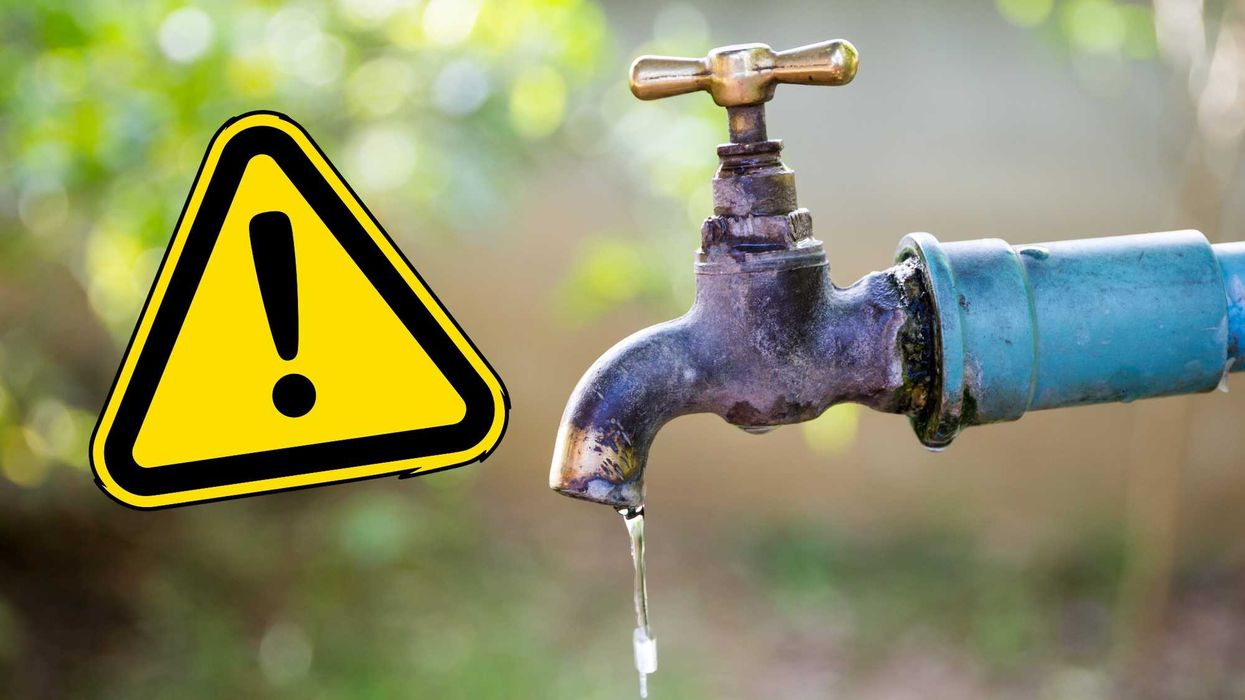 Leaking faucet with a warning sign, outdoor blurred background.