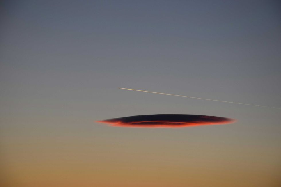 Lenticular cloud at sunset with contrail in a clear sky.