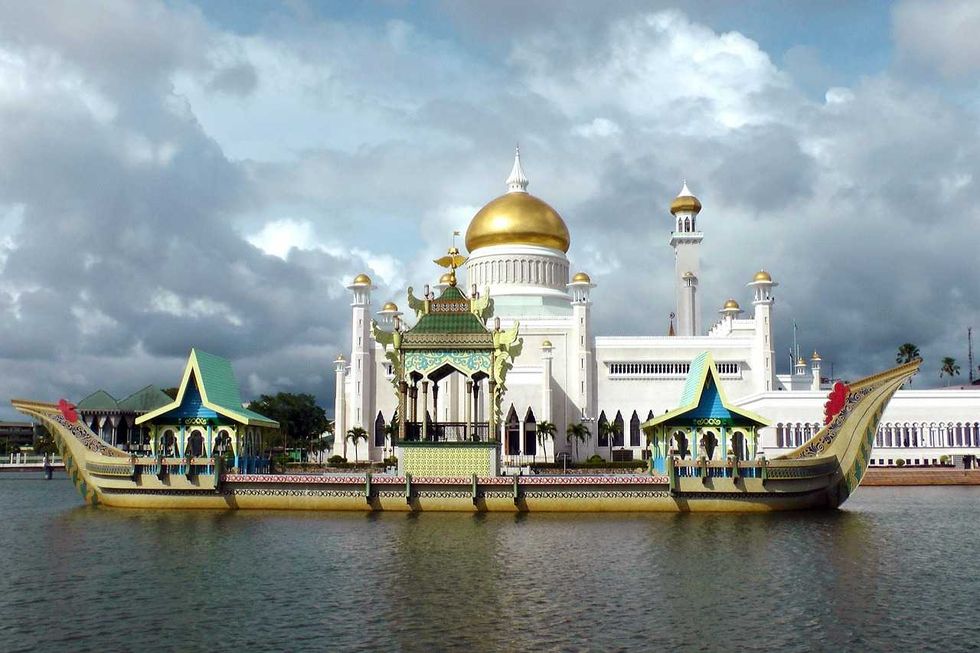 Majestic mosque with golden dome and ornate boat in front, reflected on tranquil water.