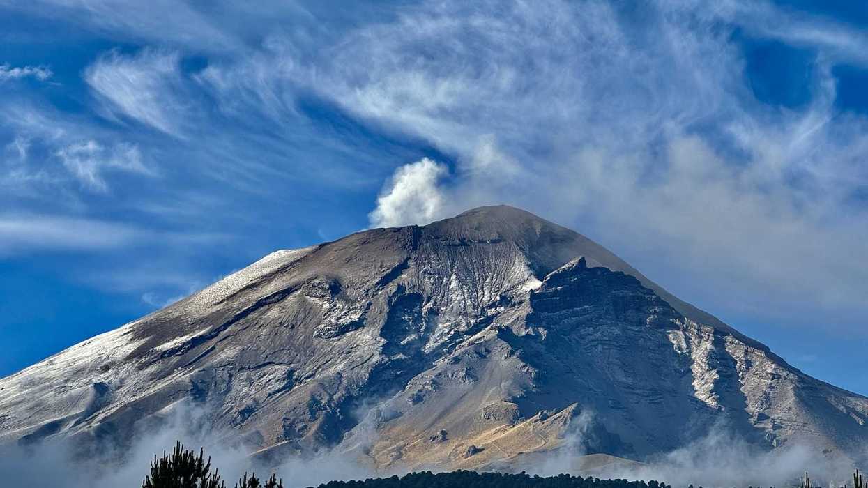 Majestic volcano with smoke under a bright blue sky and wispy clouds.