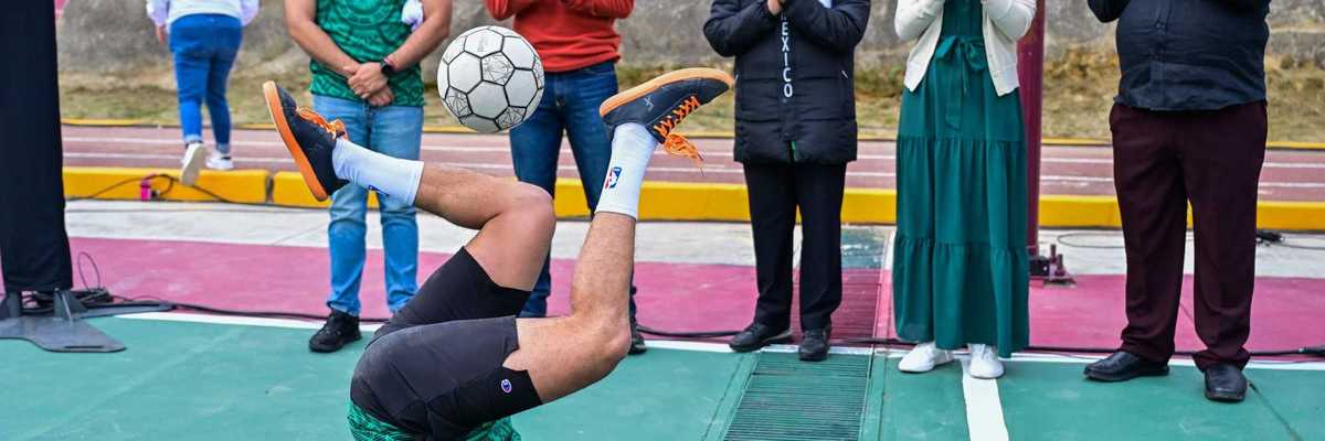 Man balances soccer ball on feet upside down while people clap.