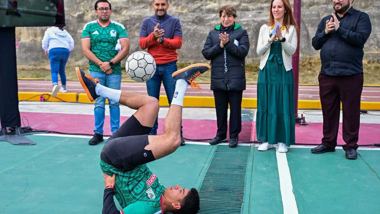 Man balances soccer ball on feet upside down while people clap.