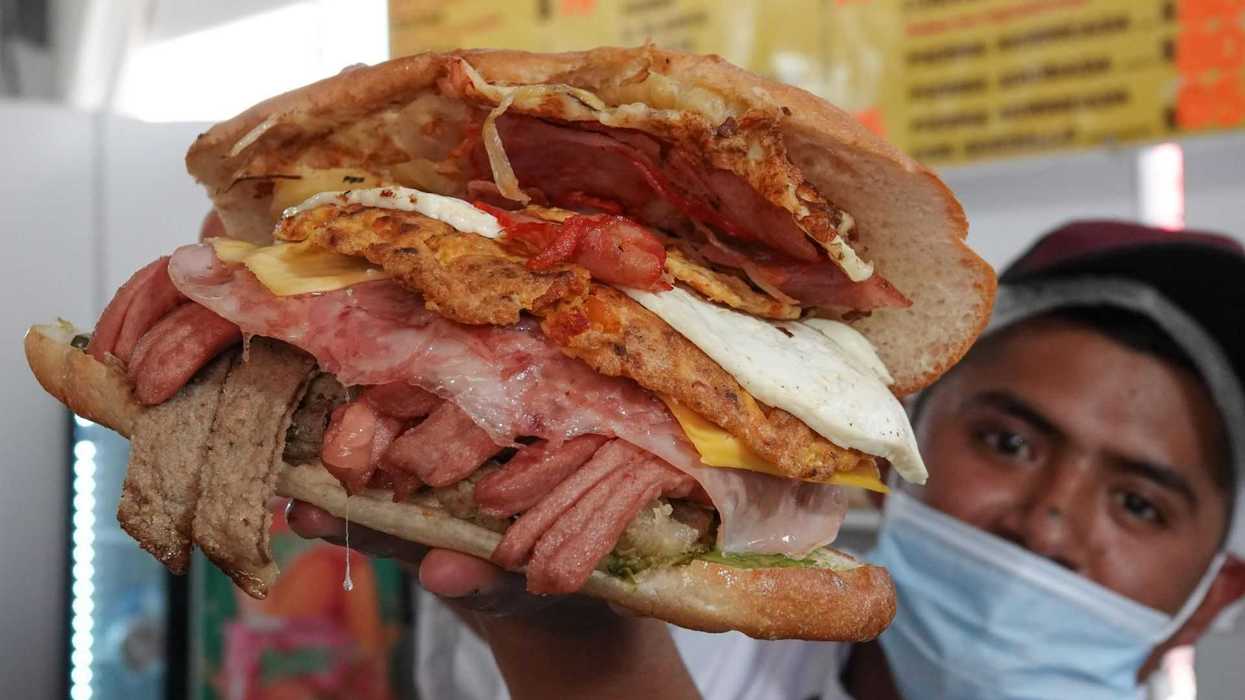 Man holding a massive sandwich with meats and fried eggs.