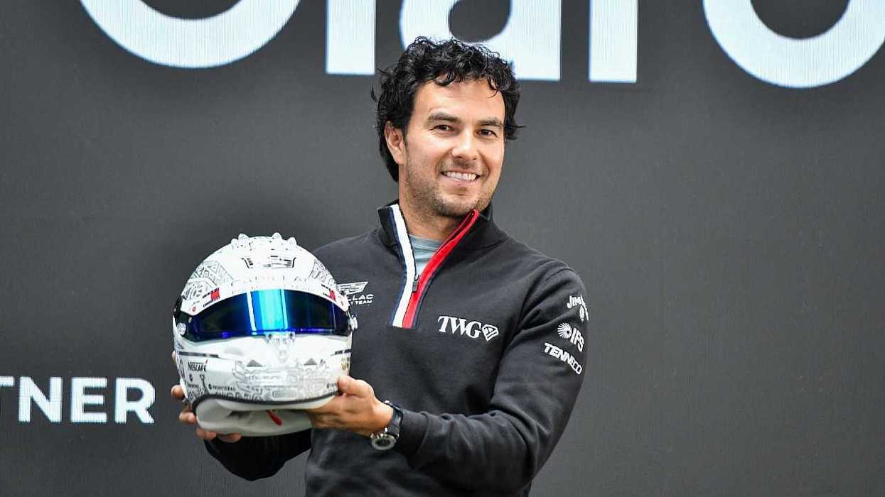 Man holding a racing helmet, smiling in front of a black and white background.