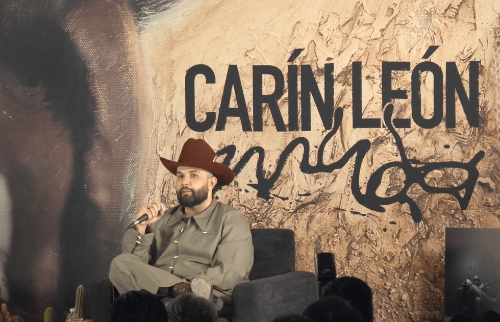 Man in a cowboy hat speaking on stage with "Car\u00edn Le\u00f3n" text in background.