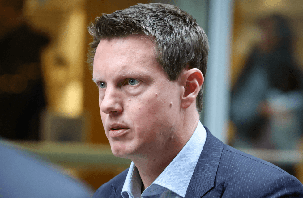 Man in a suit looking serious, with blurred background indoors.