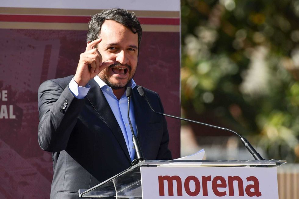 Man in a suit speaking passionately at a podium with "morena" logo.