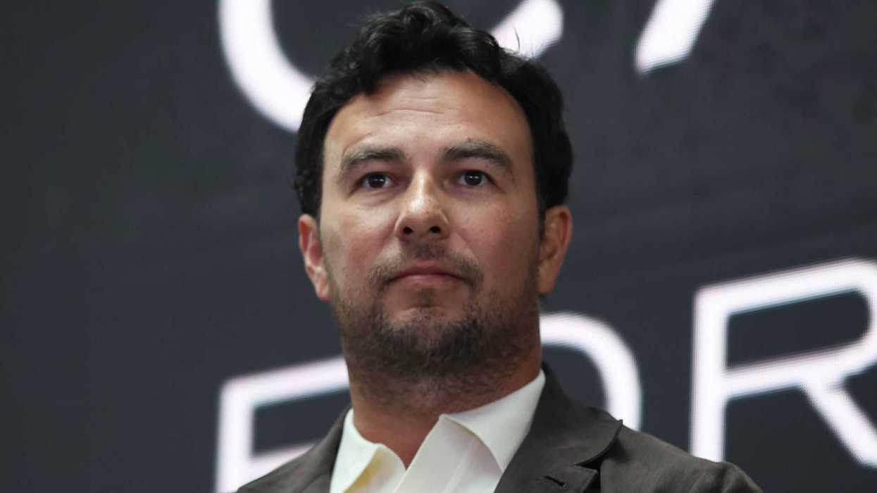 Man in a suit with a neutral expression against a dark blurred background.
