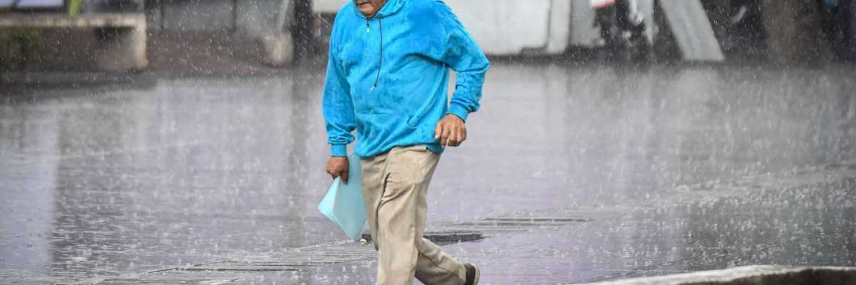 Man in blue jacket running through heavy rain on a city street.