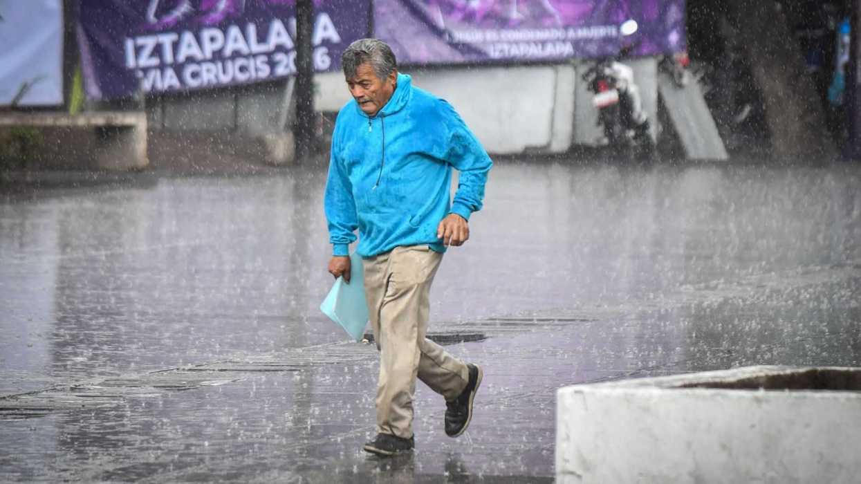 Man in blue jacket running through heavy rain on a city street.