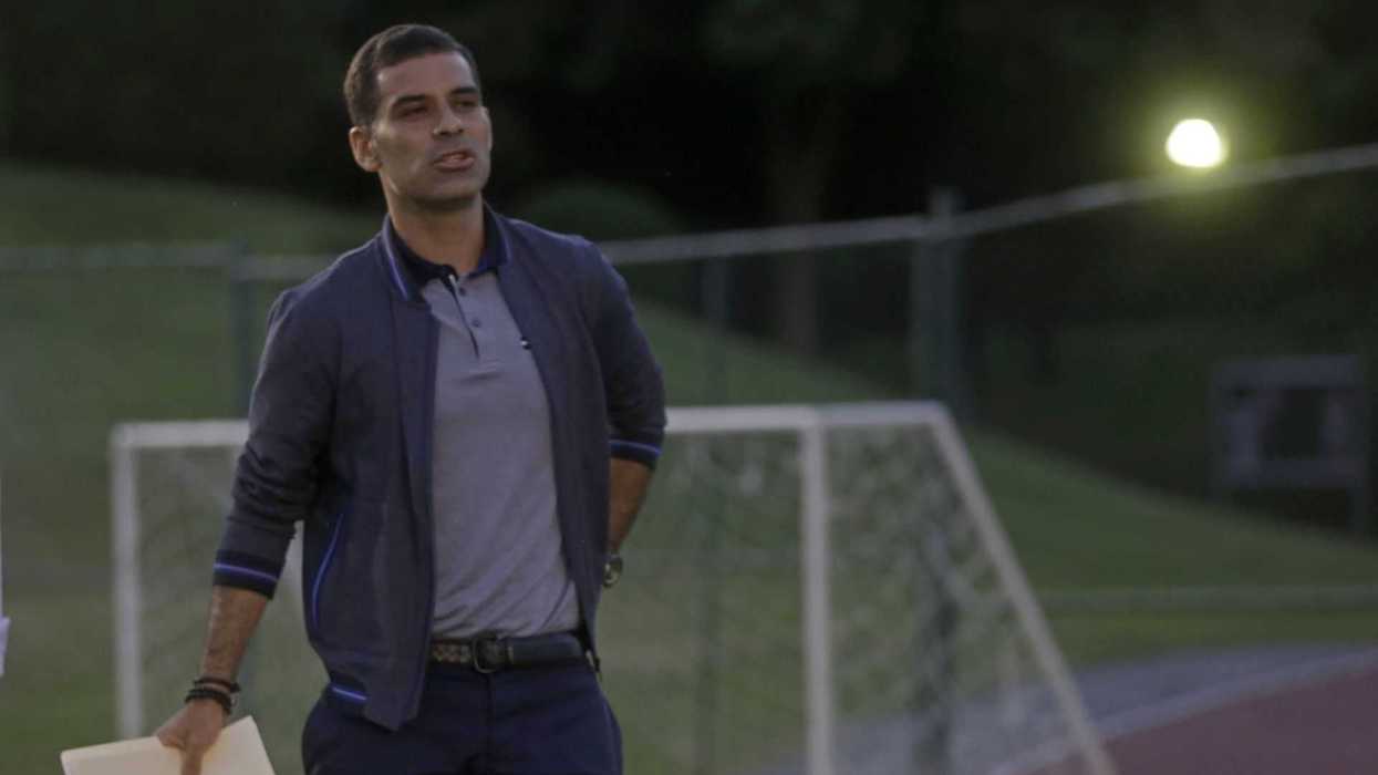 Man in jacket holding folder, standing on a field by soccer goals at dusk.