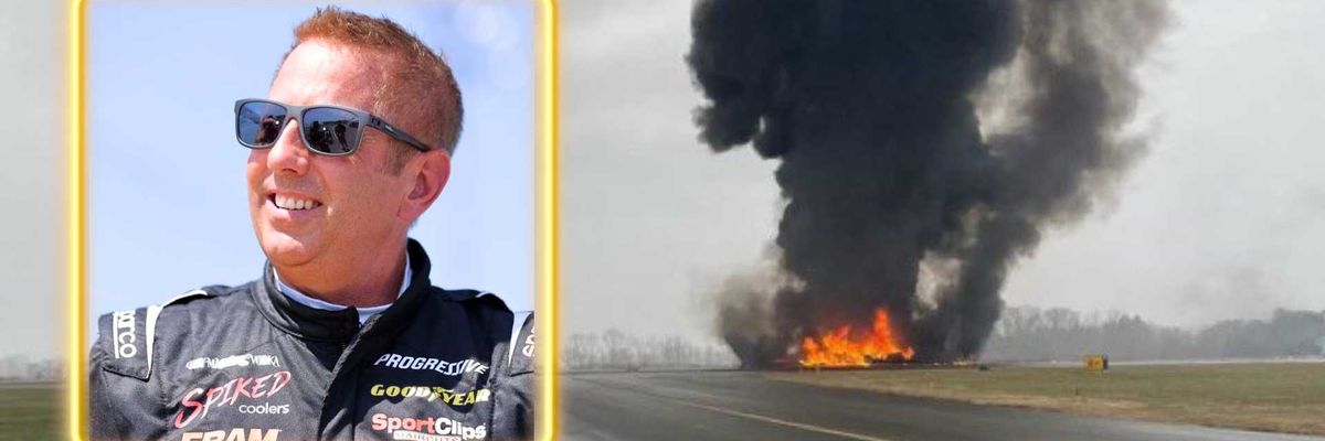 Man in racing gear; large fire and smoke on runway in background.