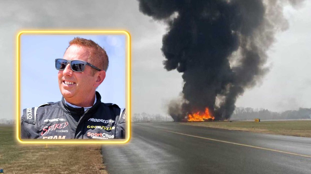 Man in racing gear; large fire and smoke on runway in background.
