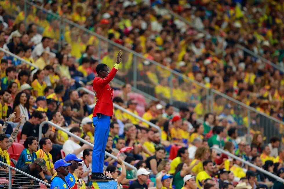 Man in red suit leading crowds in a lively, colorful stadium atmosphere.