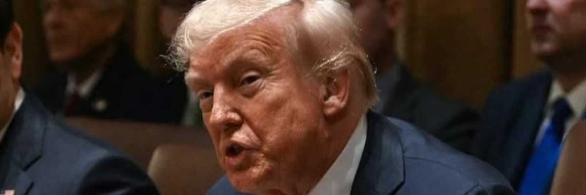 Man in suit speaking at a meeting, surrounded by other seated individuals.