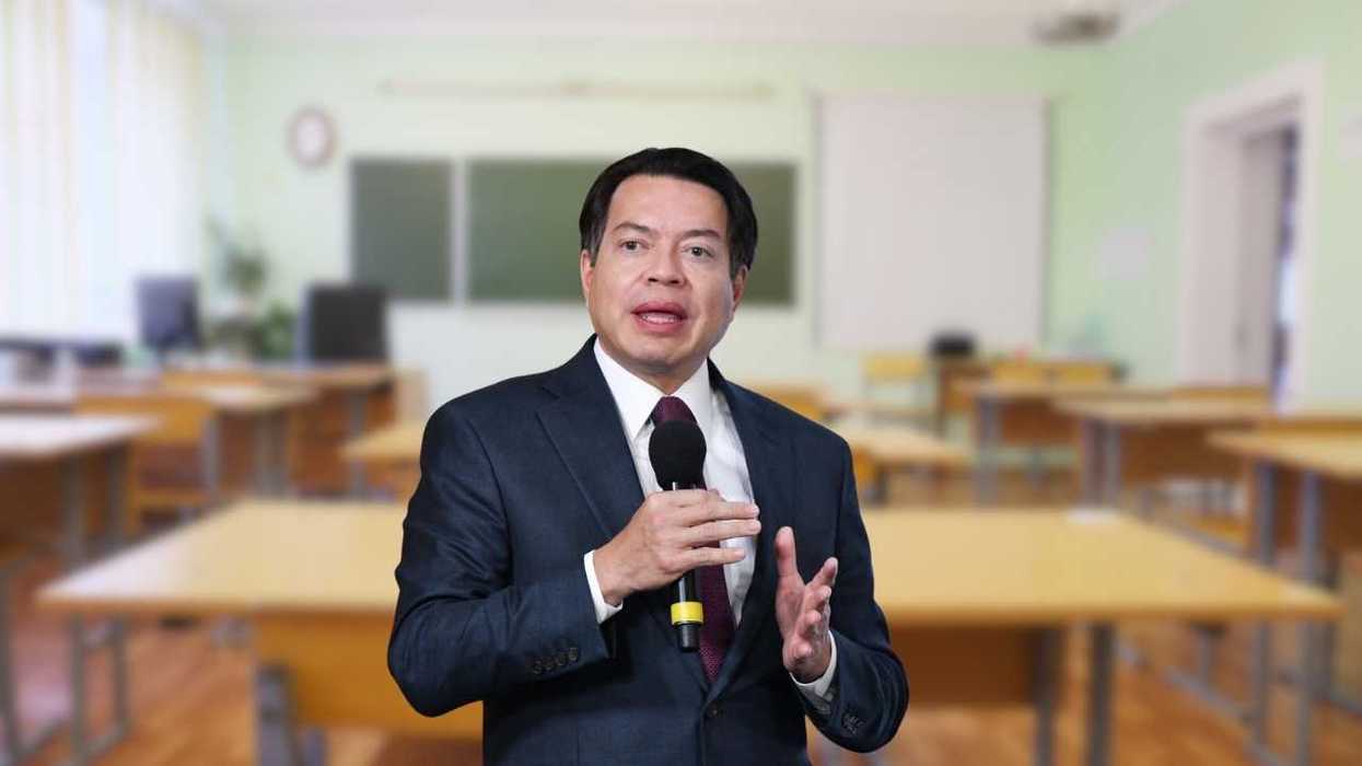 Man in suit speaking into a microphone in an empty classroom.