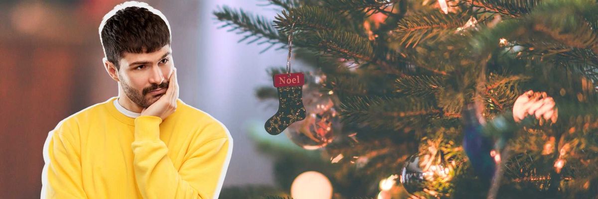 Man in yellow sweater pondering near decorated Christmas tree.