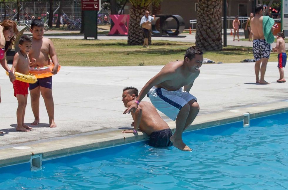 Man jumping into pool, children with floaties nearby, sunny day.