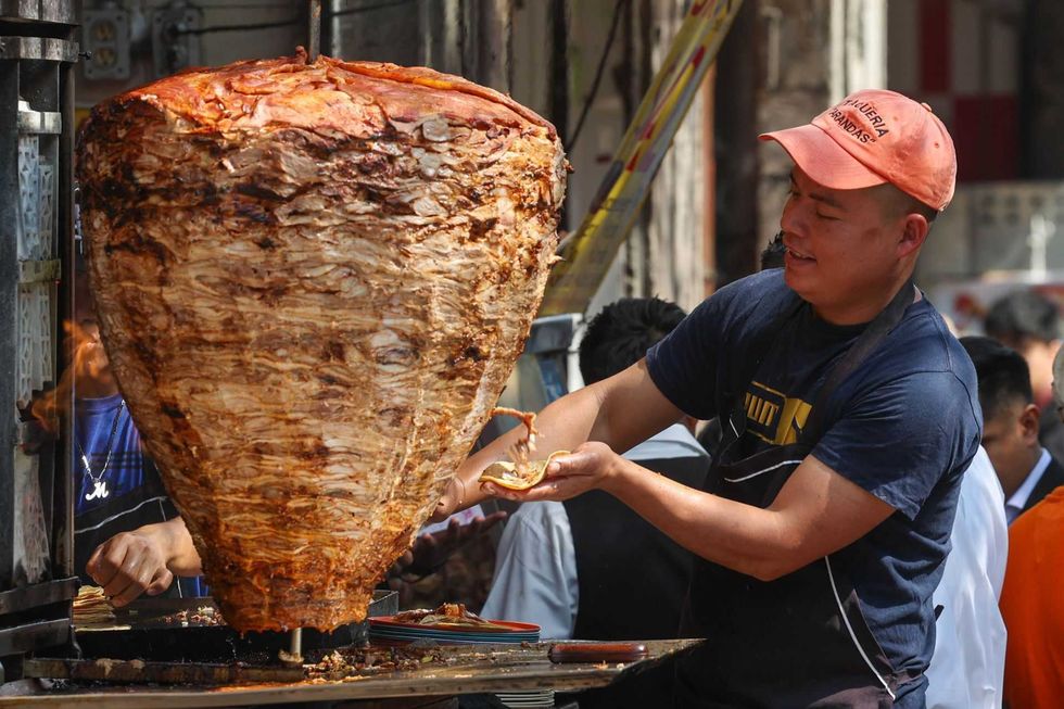 Man slicing meat from a large vertical spit at an outdoor food stand.