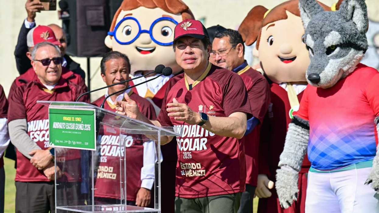 Man speaking at podium with mascots and crowd in matching maroon shirts behind him.