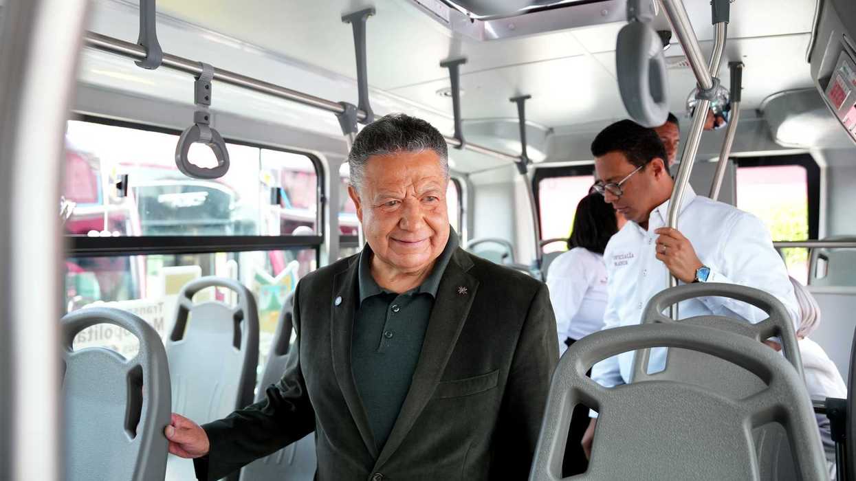 Man standing inside a bus, smiling, with other passengers in the background.