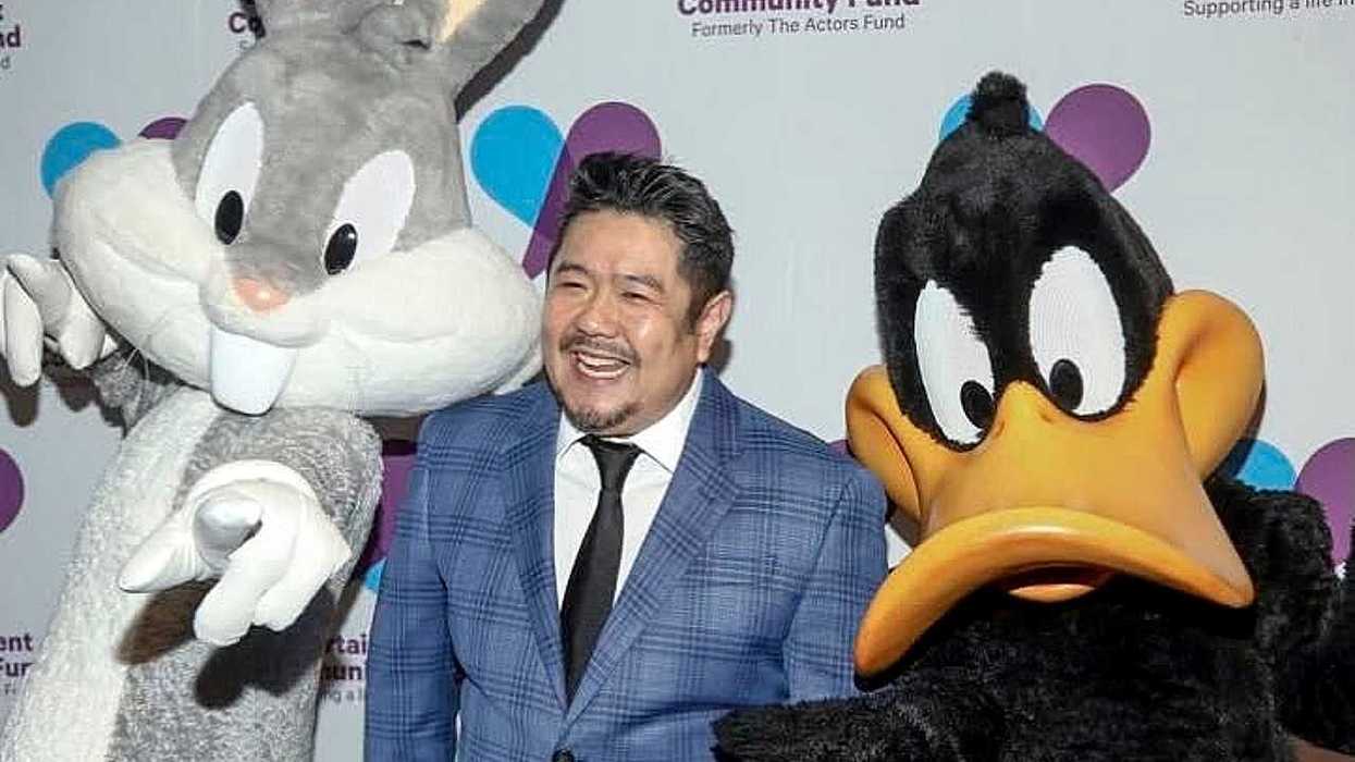 Man with Bugs Bunny and Daffy Duck mascots at an event backdrop.
