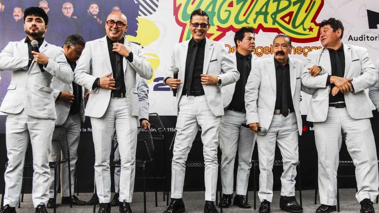 Men in matching light grey suits pose on stage with microphones.