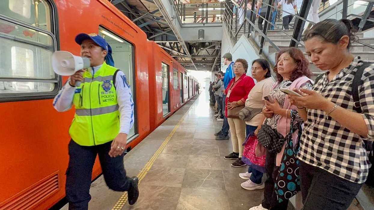 Metro guard with megaphone by orange train, people waiting on platform.