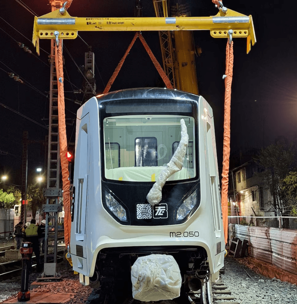 Metro train car being lifted by crane on a railway track at night.