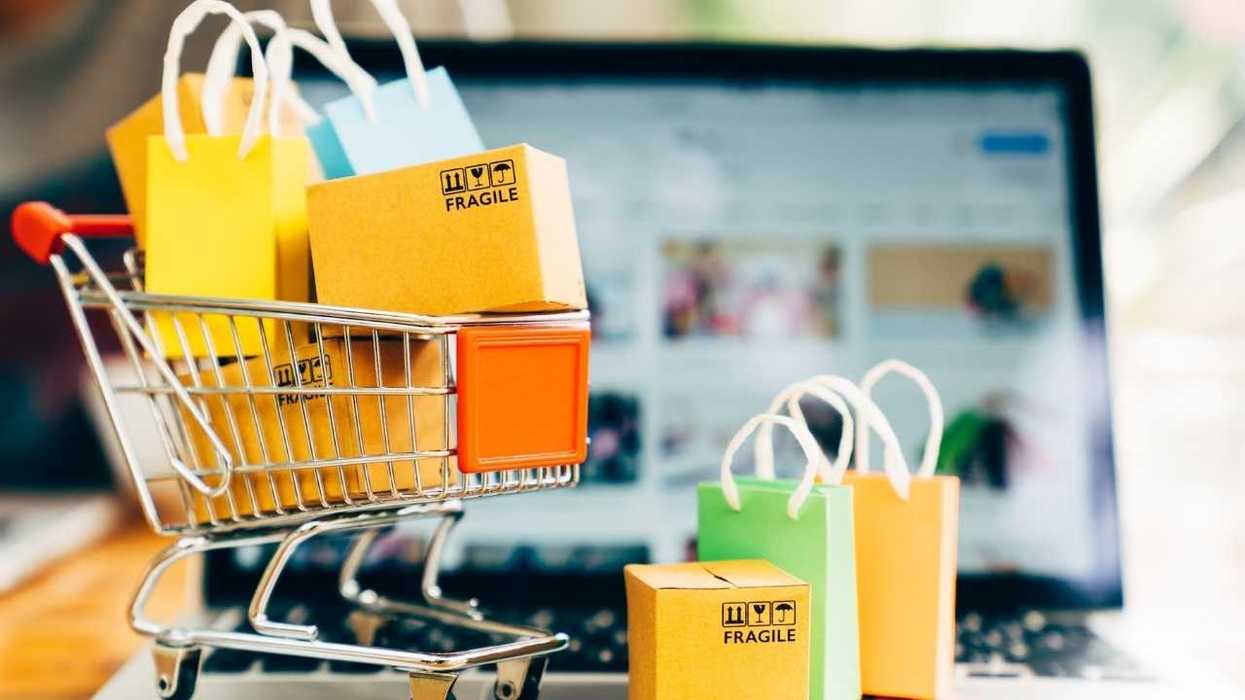 Mini shopping cart and bags in front of a laptop displaying an online store.