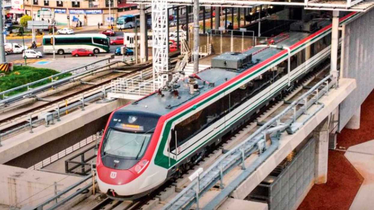 Modern commuter train with red and green stripes on elevated tracks near city streets.