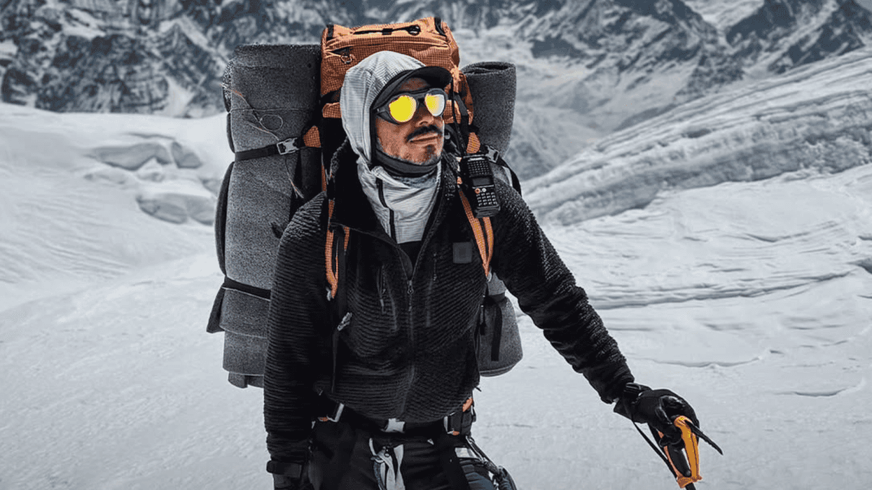 Mountaineer with gear trekking snowy mountain landscape under clear blue sky.