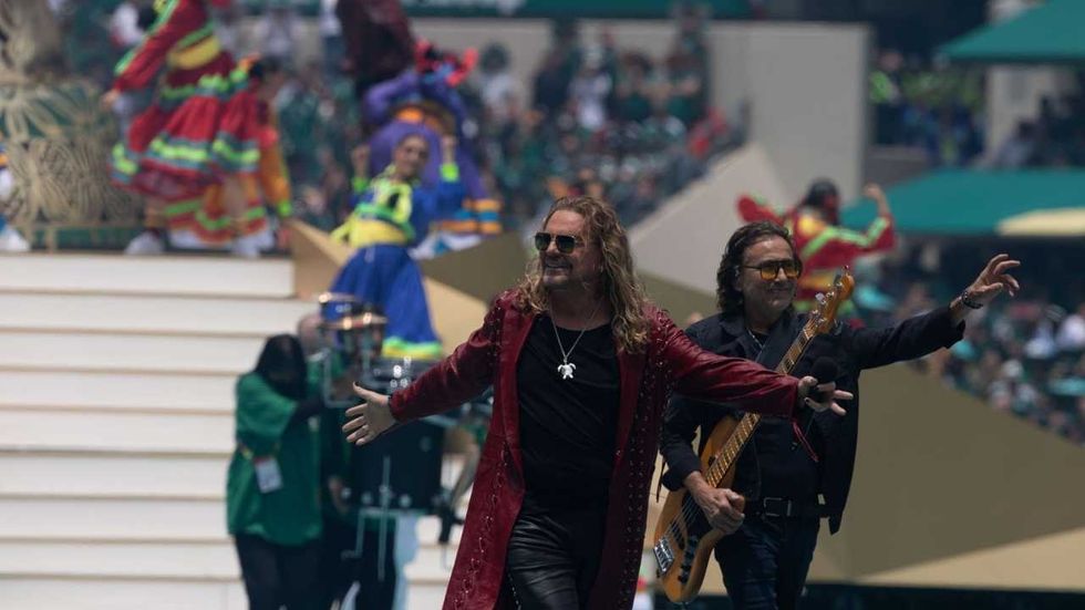 Musicians on stage with vibrant dancers in colorful traditional attire in the background.