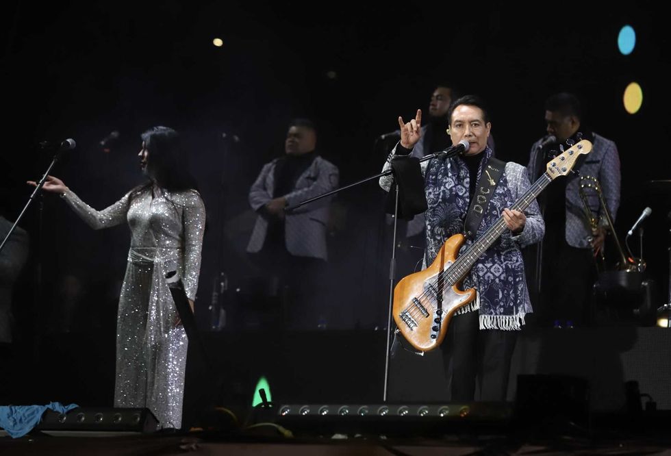 Musicians performing on stage; man with guitar, woman in shimmering dress.