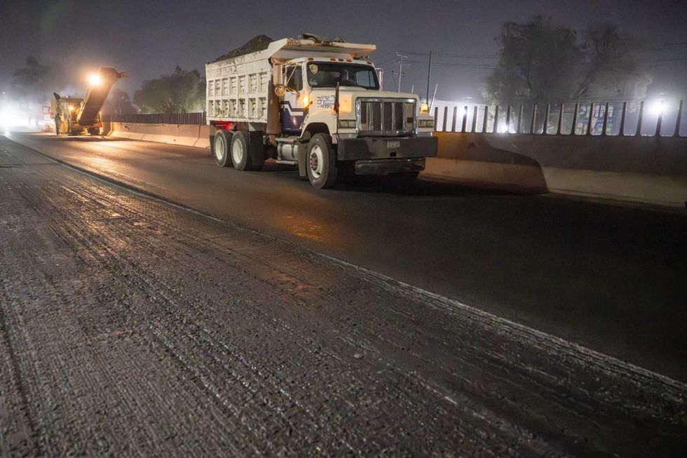 Night road construction with a dump truck and machinery working on the highway.