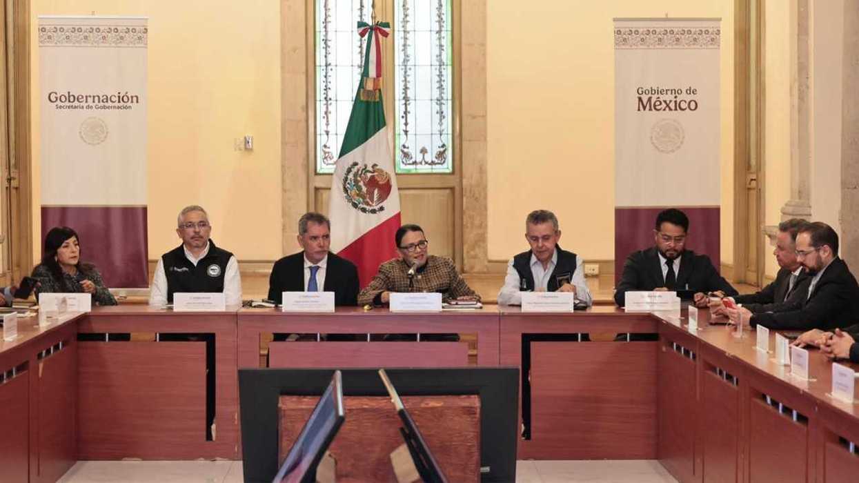 Officials at a conference table with Mexican flags and government banners behind them.