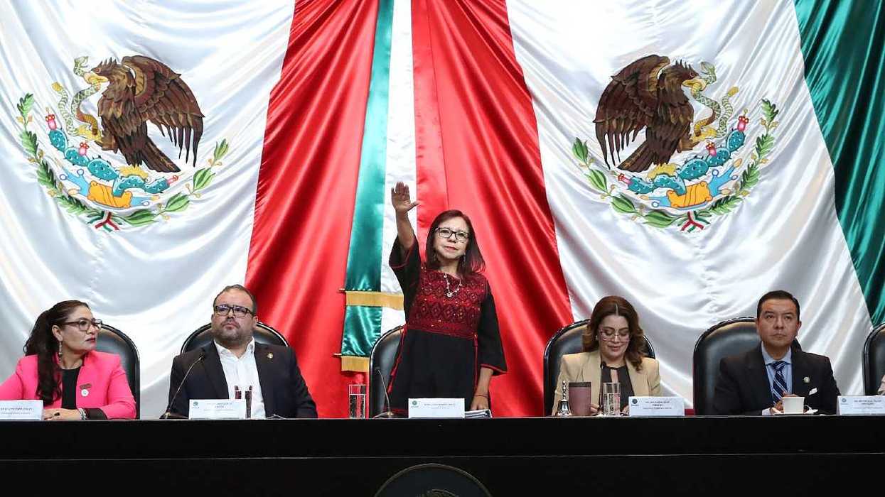 Officials seated at a table with a large Mexican flag backdrop.