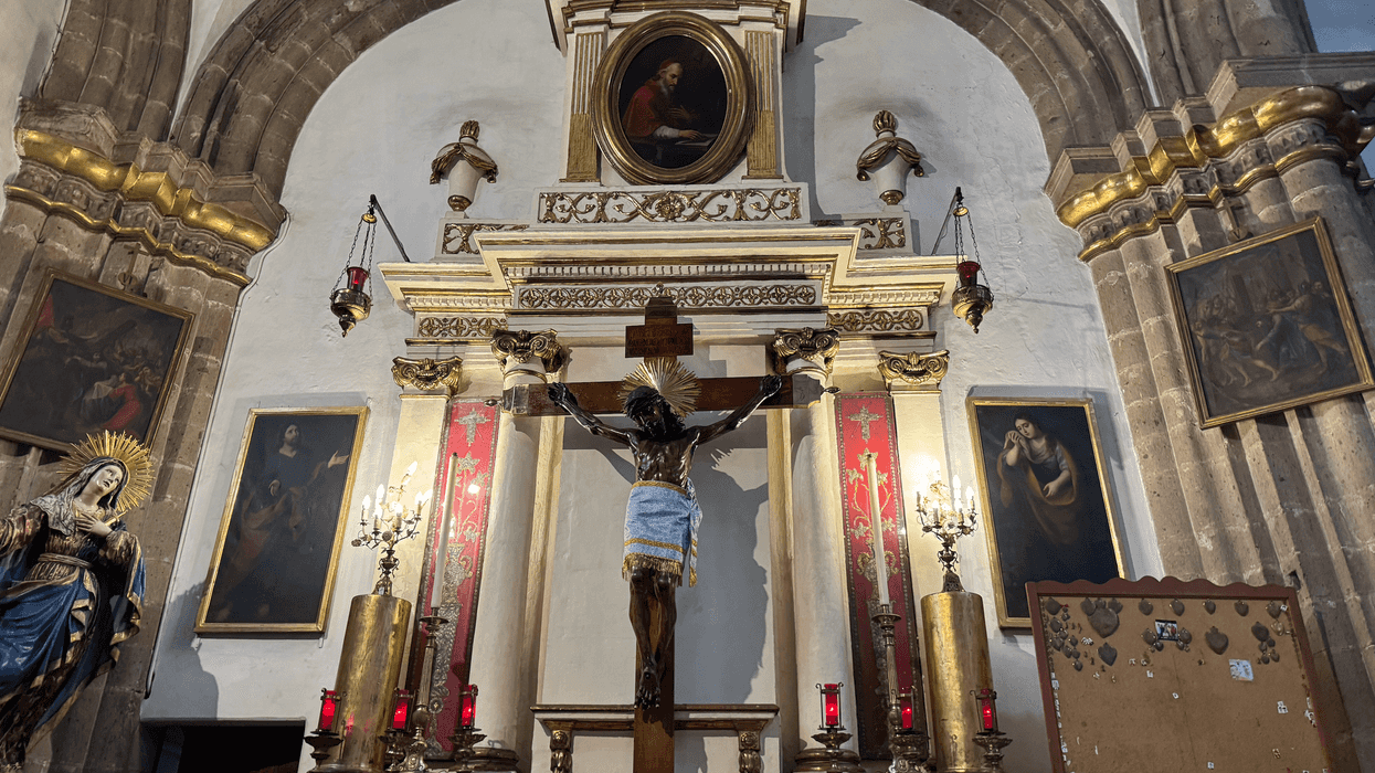Ornate church altar with crucifix and religious statues, surrounded by framed paintings.