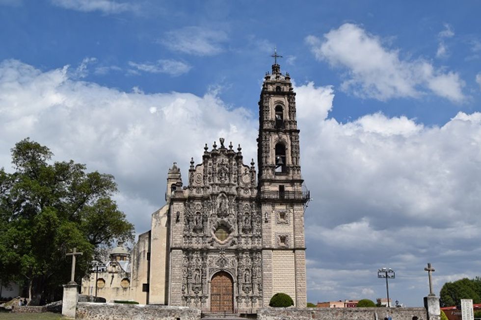 Ornate stone church facade with bell tower against a partly cloudy sky.