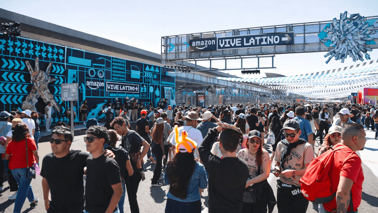Outdoor festival crowd beneath "Vive Latino" sign with vibrant blue decor and urban art.