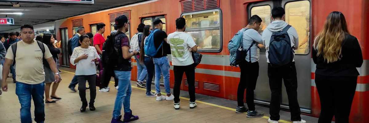 Passengers boarding an orange subway train at a station with "Martín Carrera" signage.