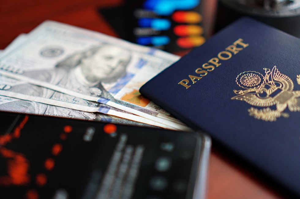 Passport, dollar bills, and smartphone on a table, symbolizing travel and finance.