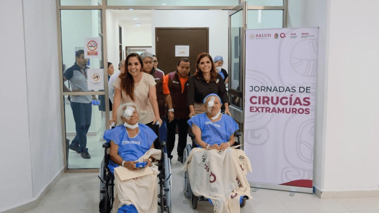 Patients in wheelchairs exit surgery area with staff assistance, near medical event banner.