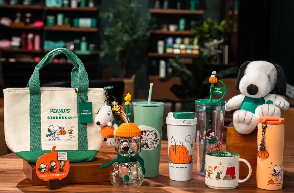 Peanuts and Starbucks merchandise with mugs, plush, and accessories on a wooden table.