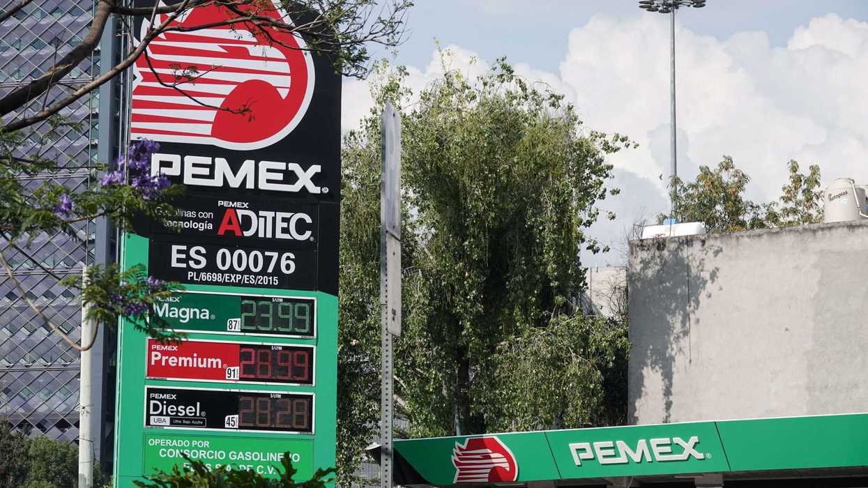 Pemex gas station sign displaying fuel prices amid trees and cloudy sky.