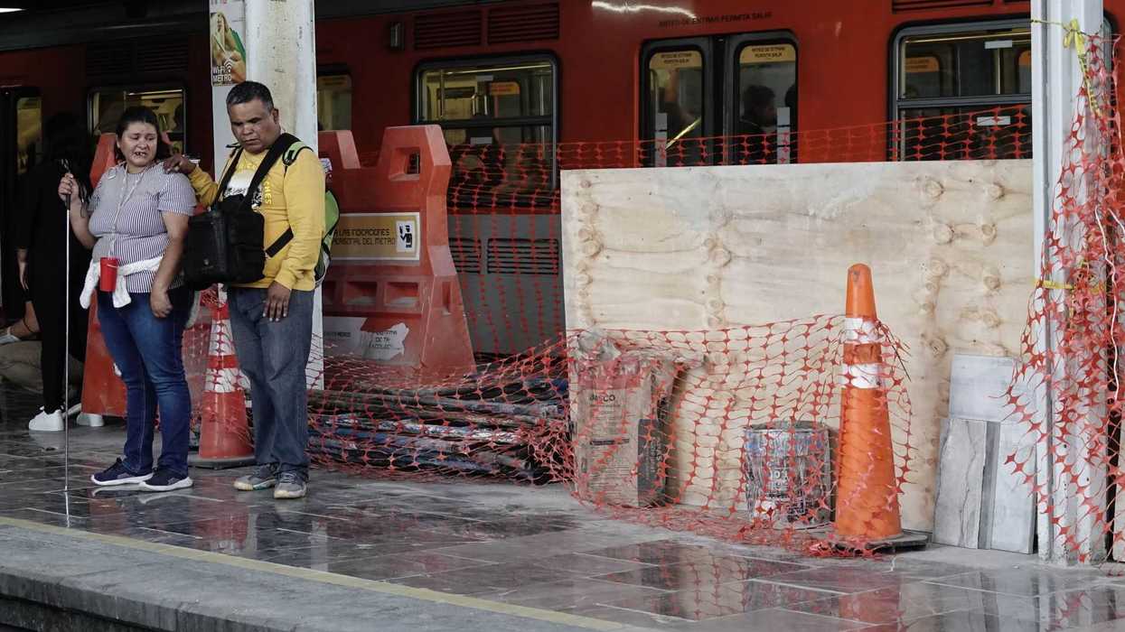 People at a subway platform near construction barriers and an orange train.