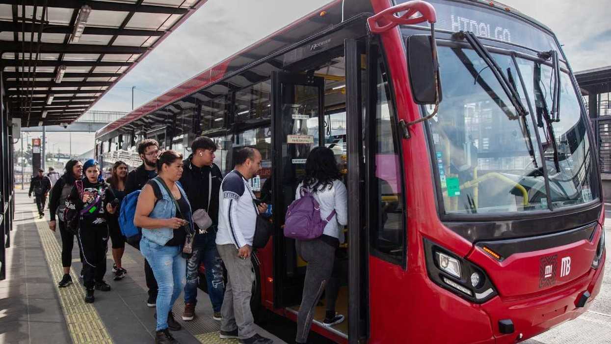 People boarding a red city bus at a transit station.